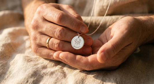 Photo d'une main qui tient doucement une médaille gravée avec le nom d'un chien, ambiance lumineuse et mélancolique, cadrage serré